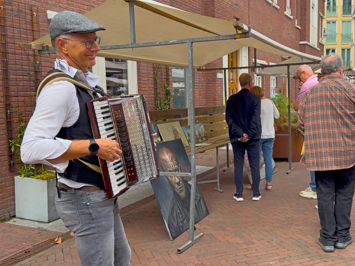 Accordeonist met pet speelt bij een kraam met schilderijen